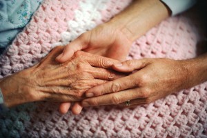 A geriatrician holds the hand of an elderly woman with arthritis.